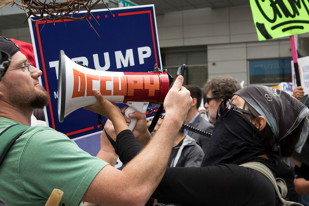 An anti-Trump protester blares music in the face of a Trump supporter. (Chloe Aiello/Denverite)