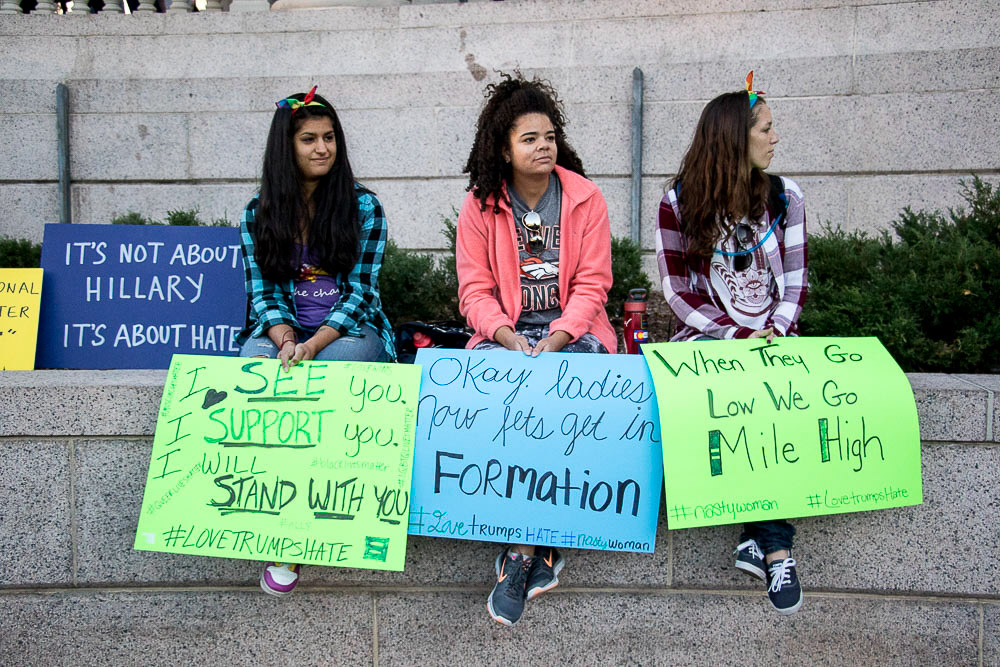 Anahita Khosravi, 26, Aisha Henry, 24, and Emerald Smith, 24 sit on a ledge in Civic Center Park to support Community for Unity after Thursday's march. (Chloe Aiello/Denverite)