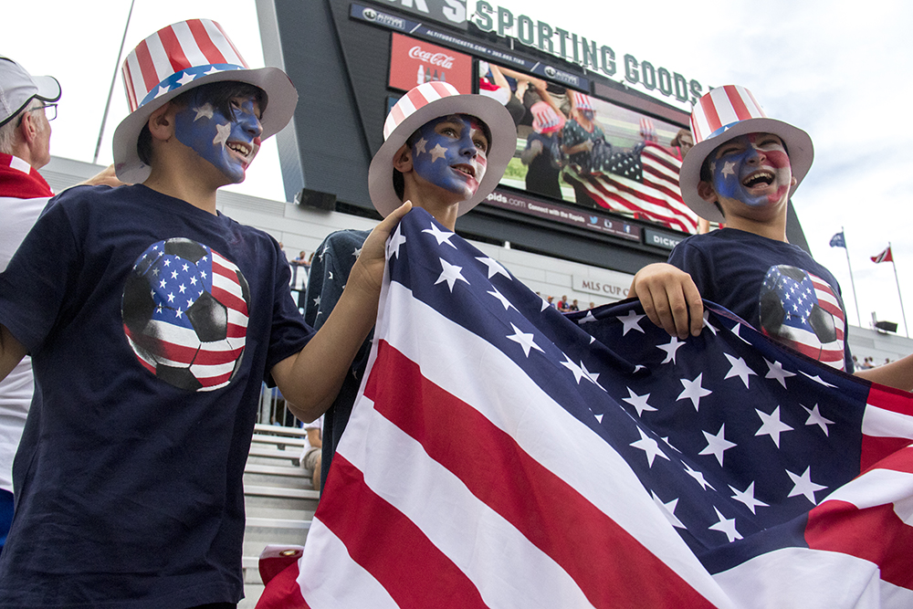 Taylan (left to right), Bodhi and Yigitcan jump up and down with an American flag as they're broadcasted on the big screen. The U.S. men's national soccer team vs Trinidad and Tobago, Dick's Sporting Goods Park, June 8, 2017.
