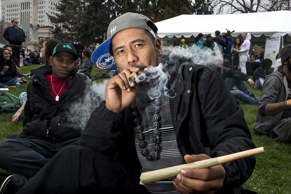 A member of the Twizted Kaskezt car club from Greeley, who asked not to be named, smokes a huge joint while holding a huge joint. Denver's 2018 Mile High 420 Festival, April 20, 2018. (Kevin J. Beaty/Denverite)
420; stoner; denver; denverite; colorado; kevinjbeaty;