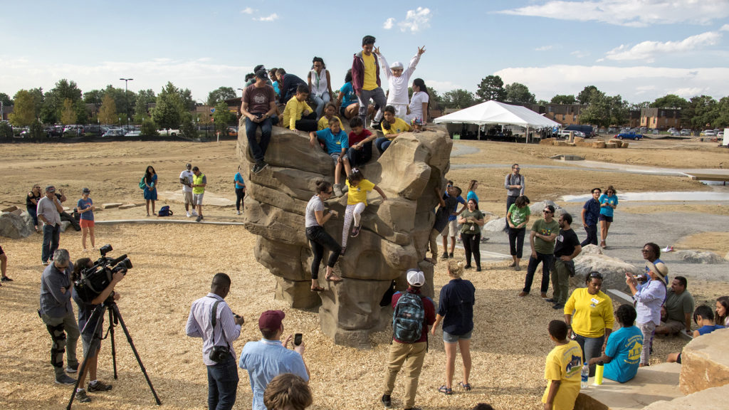 Kids climb atop a new boulder unveiled at Montbello Open Space Park, July 24, 2018. (Kevin J. Beaty/Denverite)