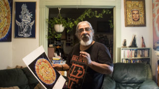 Stevon Lucero holds a print of his Mayan calendar painting at his Highland home and studio, July 29, 2018. (Kevin J. Beaty/Denverite)