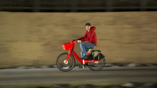 A man in a red hoodie rides a red Jump bike on the Cherry Creek Trail, Aug. 20, 2018. (Kevin J. Beaty/Denverite)