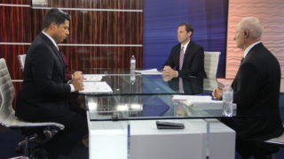 U.S. Rep. Mike Coffman (right) sits next to to Jason Crow (middle) while Univision Colorado Anchor Juan Carlos Gutierrez looks at notes before the start of a debate on Monday, Oct. 22, 2018, in Denver. (Esteban L. Hernandez/Denverite)