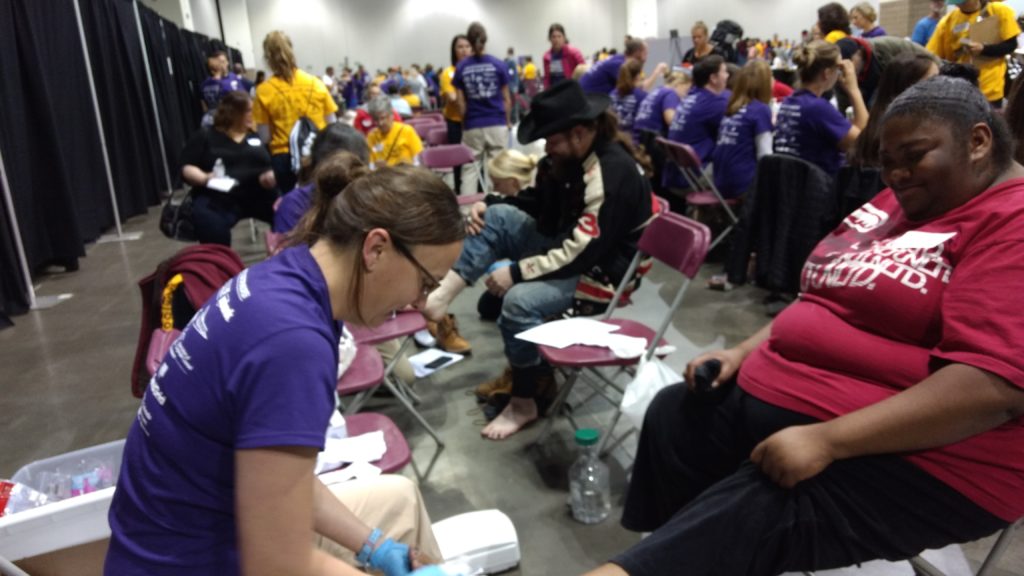 Regis University nursing student Dana Zimmer checks the feet of shelter resident Tracy Davis during Project Homeless Connect. The event puts a variety of resources in one place -- the Colorado Convention Center -- for people experiencing homelessness. (Donna Bryson/Denverite)