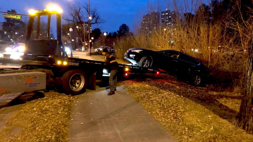 A tow truck driver pulls a wrecked vehicle off of a hill just above the Cherry Creek Trail. (David Sachs/Denverite)