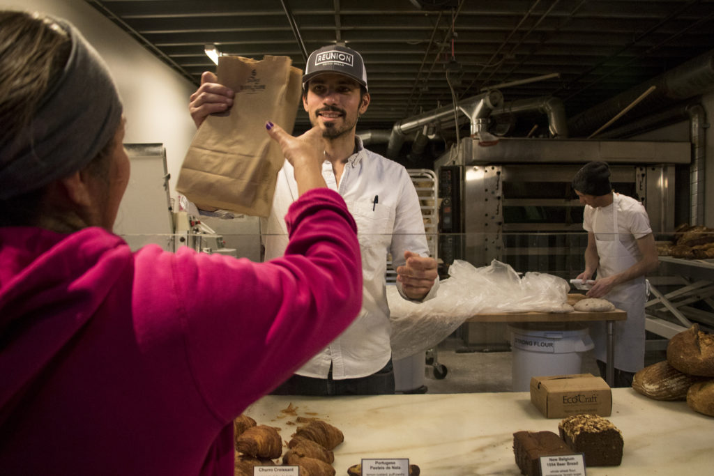 Reunion Bakery founder Ismael De Sousa helps a customer during his shop's soft opening at The Source in RiNo, Five Points, Jan. 22, 2019. (Kevin J. Beaty/Denverite)