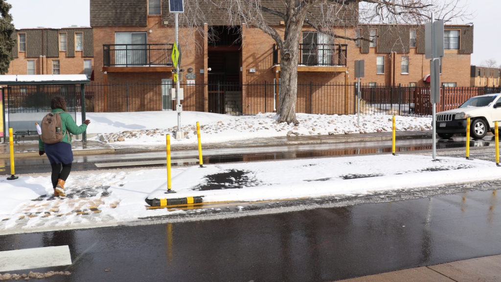 A woman crosses using Albrook Drive in Montbello using a pedestrian refuge. (David Sachs/Denverite)