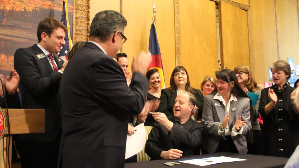 Gov. Jared Polis (center) shares a pen after signing an executive order while surrounded by supporters on Wednesday, Jan. 23, 2019, at the Capitol. (Esteban L. Hernandez/Denverite)
