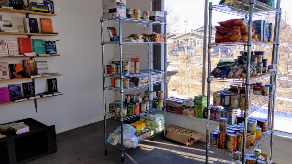 Books and food on the shelves at Counterpath, a publisher and exhibition space where the East Colfax Neighborhood Association has set up a food pantry. (Donna Bryson/Denverite)