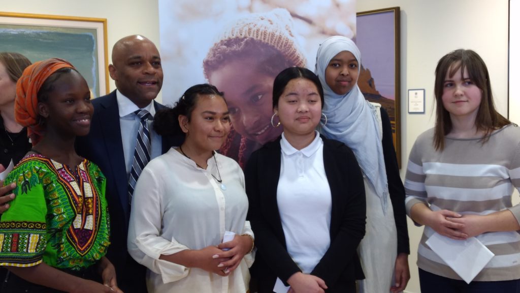 Mayor Michael B. Hancock in background with Place Bridge Academy students (from left to right) Grace Yose, Emmy Ramos, Salma Yusuf, Ro Win Na and Irina Vorobey at a Denver Human Services news conference. Place Bridge is one of three Denver Public Schools where DHS social workers are based.