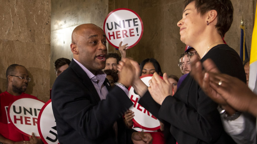Mayor Michael Hancock locks hands with City Councilwoman Robin Kniech during a press conference on a city bill to increase minimum wage for city workers, Feb. 14, 2019. (Kevin J. Beaty/Denverite)