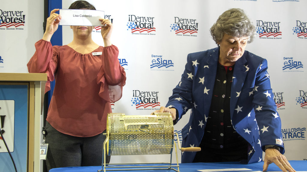 Jocelyn Bucaro (left), Deputy Director of Elections, holds up a candidate's name before she sticks it in a bingo mixer as the department holds a lottery to determine candidate order on the upcoming municipal election ballots, March 14, 2019. (Kevin J. Beaty/Denverite)