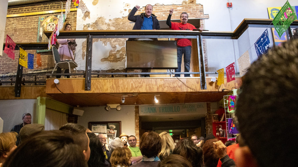 Gov. Jared Polis (left) raises a fist alongside Ramon Del Castillo during Denver's annual Cesar Chavez Day celebration at Su Teatro on Santa Fe Drive, March 30, 2019. (Kevin J. Beaty/Denverite)