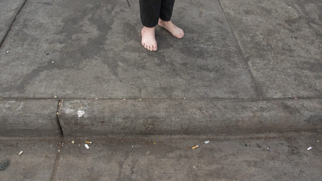 A woman stands barefoot outside of the Denver Rescue Mission, April 17, 2019. (Kevin J. Beaty/Denverite)