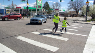 Lindsey Rosendahal and her son, Anders, runs across Federal Boulevard during a traffic slowing demo put on by Vision Zero and WalkDenver in Denver's Regis neighborhood, April 27, 2019. (Kevin J. Beaty/Denverite)