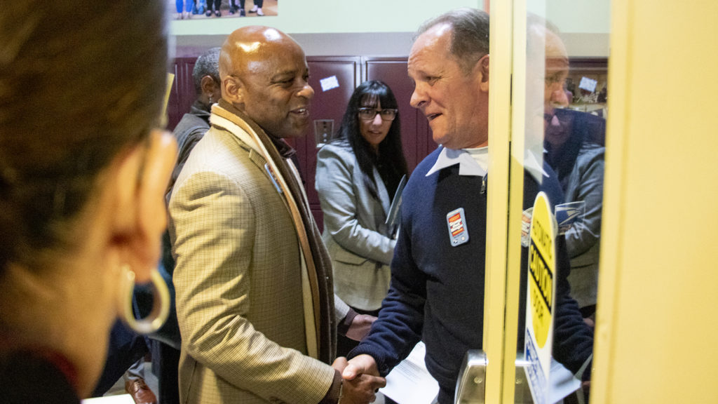 Mayor Michael Hancock shakes hands with U.S. Postal Service letter carrier Jeff Frey on a tour of Metro Caring, May 9, 2019. (Kevin J. Beaty/Denverite)