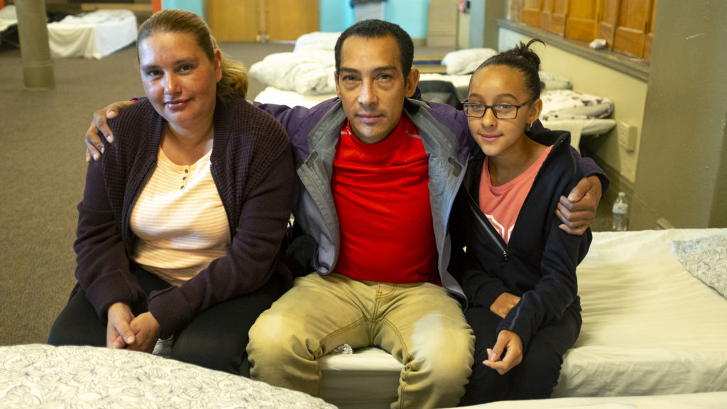 Victor Inestroza poses for a portrait with Maria Jeanette (left) and his daughter, Marta, on a cot in Denver Community Church of Christ's basement, May 14, 2019. (Kevin J. Beaty/Denverite)