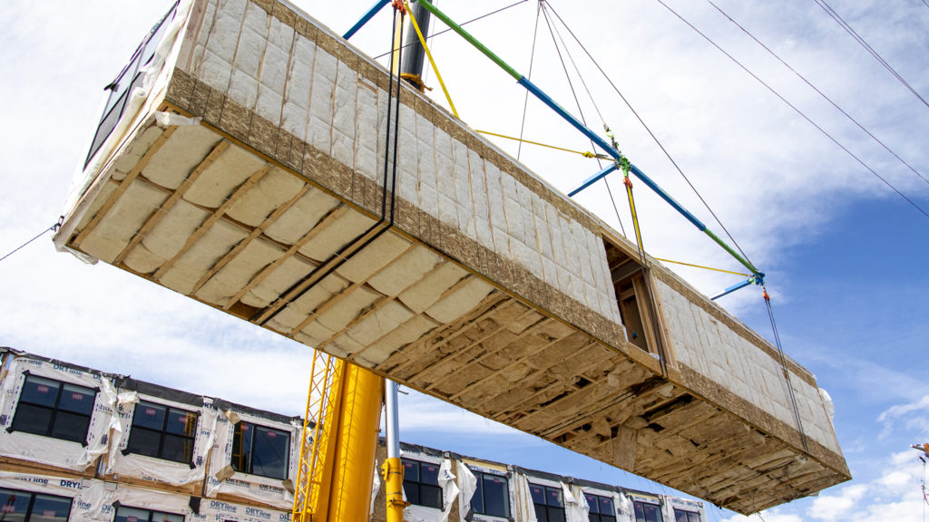 A prefab apartment section is lifted onto the next story of 1775 Federal Blvd., June 25, 2019. (Kevin J. Beaty/Denverite)