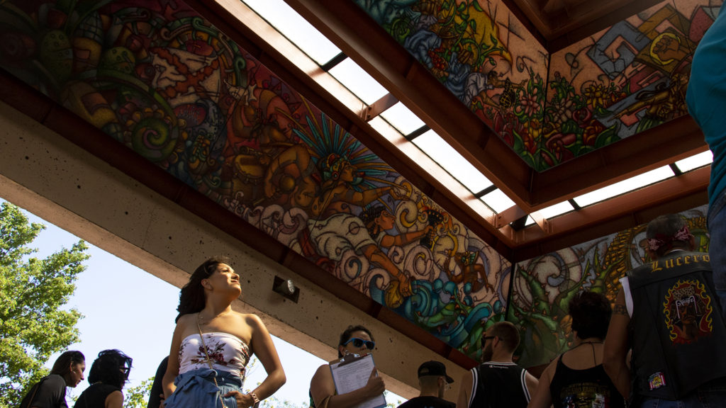 Cruisers hang out beneath the pyramid at La Raza (or Columbus) Park before a cruise down Federal Boulevard. Aug. 25, 2019. (Kevin J. Beaty/Denverite)