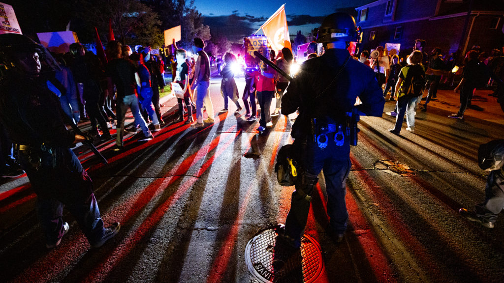 Aurora Police officers make a line in the street as immigration activists march on the home of Johnny Choate, GEO Group's lead of their contract immigration jail in Aurora. Sept. 19, 2019. (Kevin J. Beaty/Denverite)