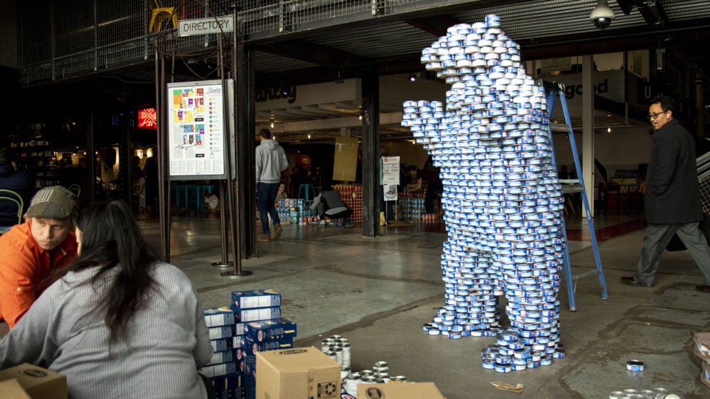 Aileen Tang and Luke Buranen build a big blue bear during We Don't Waste's "Can-struction" show at Stanley Marketplace. Nov. 15, 2019. (Kevin J. Beaty/Denverite)