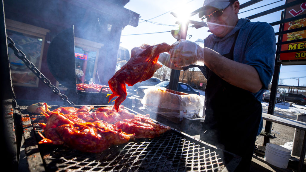 Javier Gonzales throws chicken on a series of grills in front of Los Alambres on Morrison Road, Westwood. Jan. 2, 2020. (Kevin J. Beaty/Denverite)