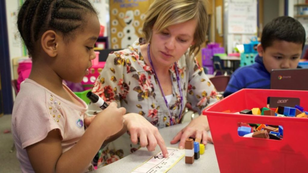 A kindergarten teacher at Kenton Elementary in Aurora helps a student practice saying and writing numbers. (Yesenia Robles/Chalkbeat)