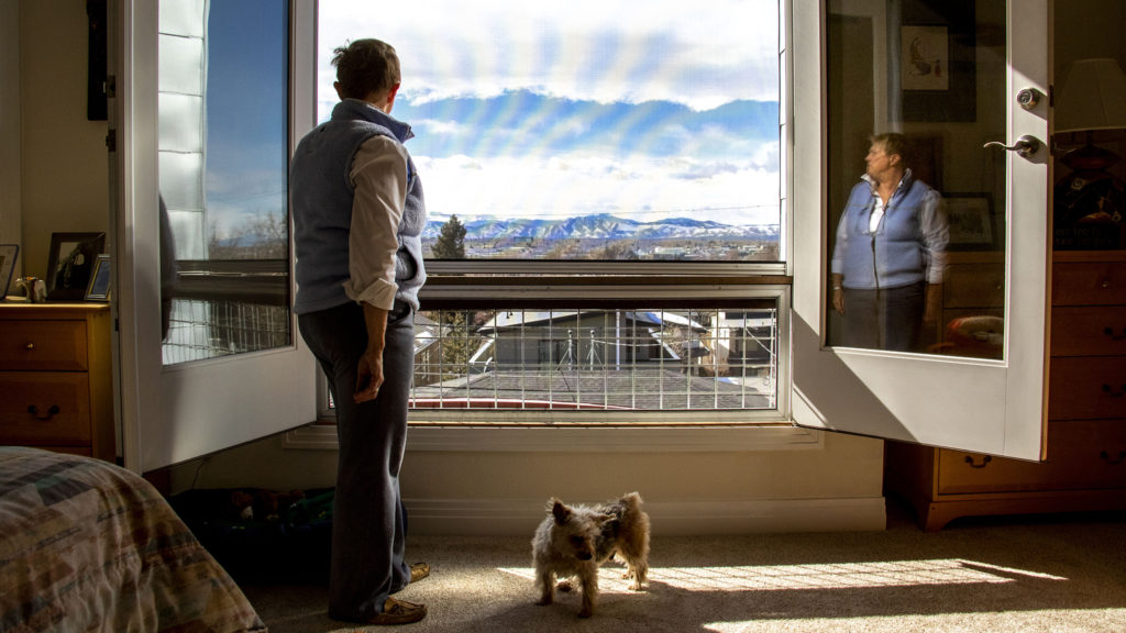 Sandy Pierce looks out onto the view from her home in Denver's Rosedale neighborhood as her dog, Buckaroo, stands by. Feb. 27. 2020. (Kevin J. Beaty/Denverite)