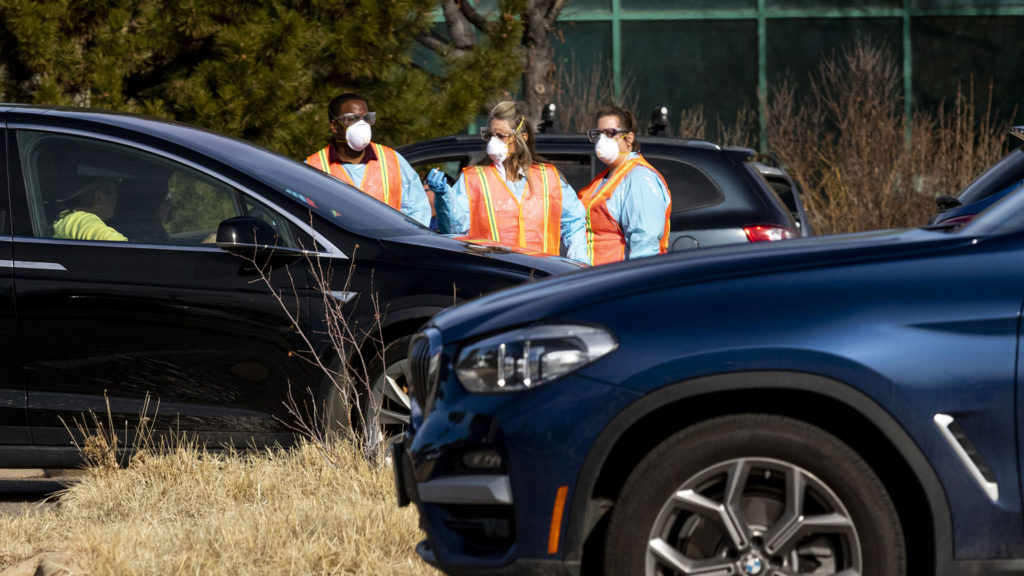 Workers survey people in cars waiting to be tested at the Colorado Department of Health and Environment's COVID-19 testing station in Lowry. March 11, 2020. (Kevin J. Beaty/Denverite)