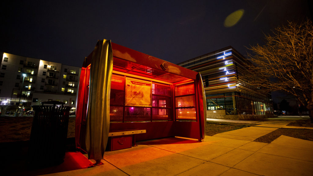 A solar-powered bus shelter is illuminated in candy-apple red. West Colfax Avenue, March 12, 2020. (Kevin J. Beaty/Denverite)