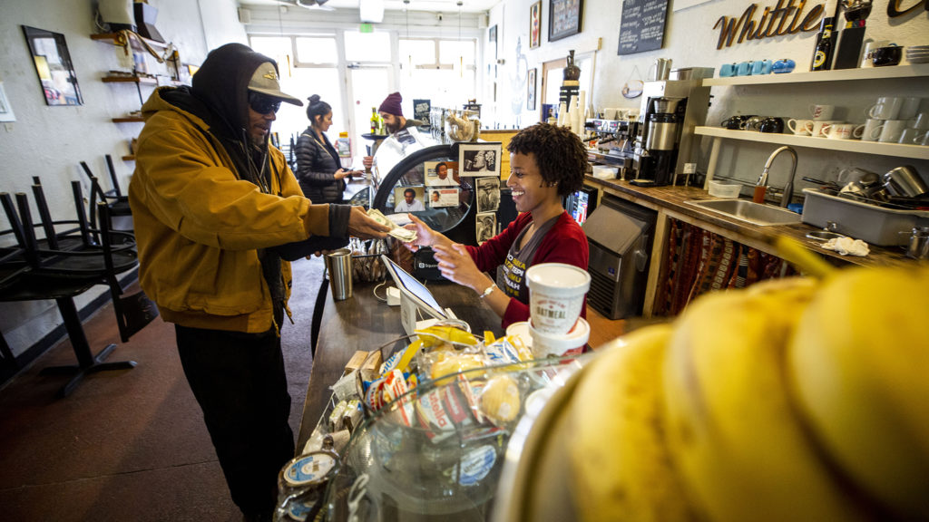 Mark Dishmon pays Sarafina Kidane for coffee at Whittier Cafe, which is closed to diners but open for to-go orders. March 17, 2020. (Kevin J. Beaty/Denverite)