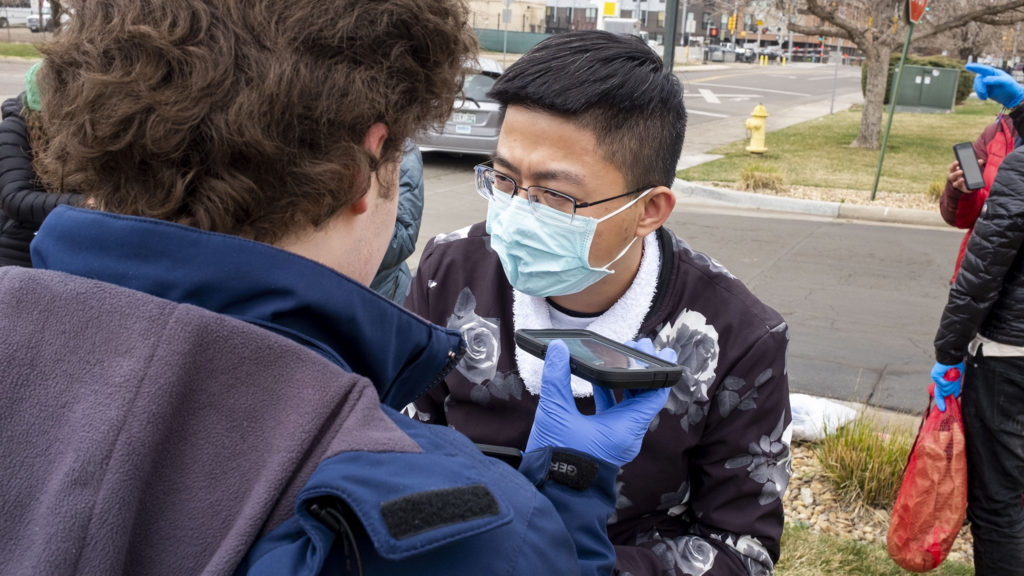 Casa De Paz volunteer Matthew Donohue speaks Mandarin to help a recently freed migrant get in touch with family elsewhere in the U.S. March 27, 2020. (Kevin J. Beaty/Denverite)