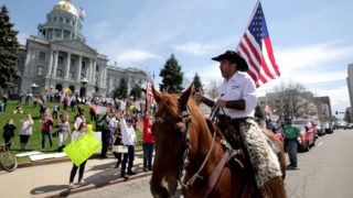 Couy Griffin rides a horse up Lincoln Street as protesters demand the end to Colorado's stay-at-home order at the state Capitol building. April 19, 2020. (Kevin J. Beaty/Denverite)