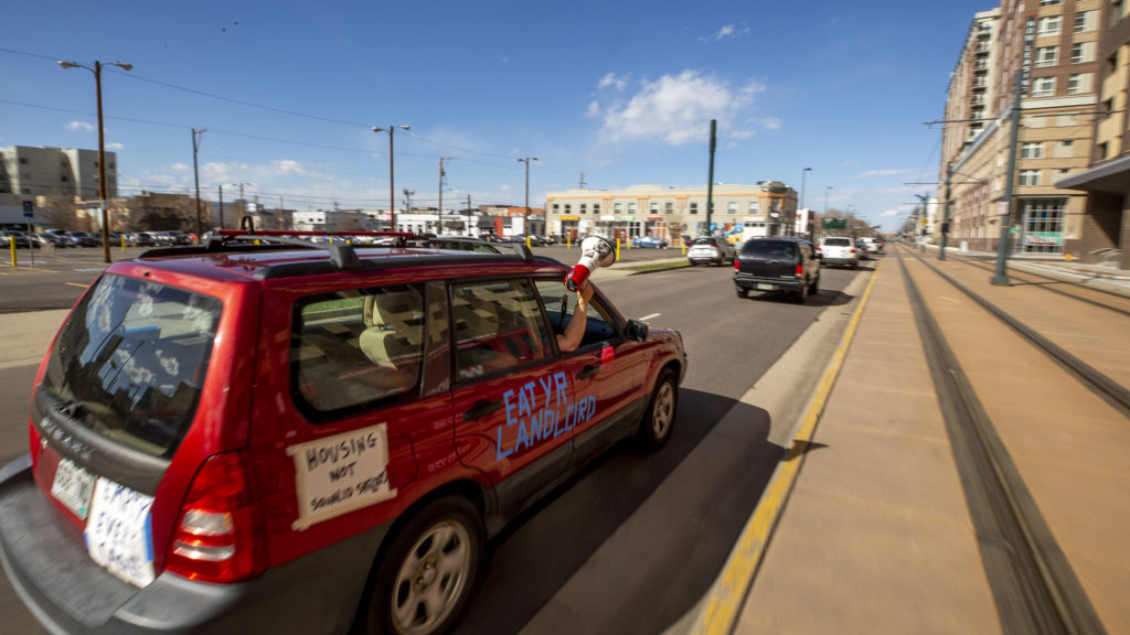 A woman yells into a bullhorn in a caravan of protest cars demanding a rent and mortgage pause, among other things. April 25, 2020. (Kevin J. Beaty/Denverite)