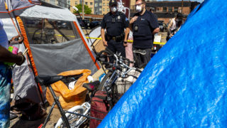Authorities tell residents of an encampment near the intersection of California and 21st Streets that they must move or else go to jail. May 27, 2020. (Kevin J. Beaty/Denverite)