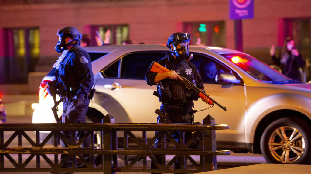 A policeman in riot gear holds a gun as protesters react to the killing of George Floyd. May 28, 2020. (Kevin J. Beaty/Denverite)