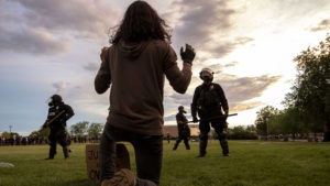 A protester kneels before officers after Aurora Police forcibly cleared the municipal building lawn at the end of a series of rallies demanding justice for Elijah McClain. June 27, 2020.