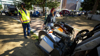 A protester attempts to stop city officials from conducting a forced cleanup of encampments at Lincoln Park, across Lincoln Street from the Capitol. July 29, 2020.
