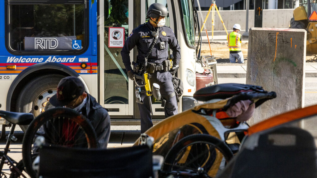 A state police officer stands ready with nonlethal munitions as city officials conduct a forced cleanup of encampments at Lincoln Park, across Lincoln Street from the Capitol. July 29, 2020.