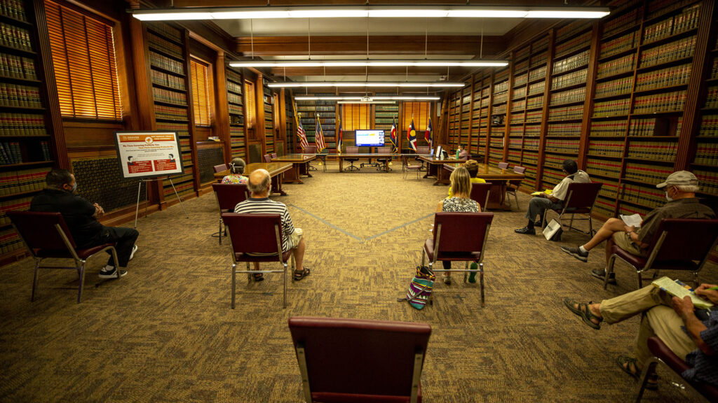 Residents watch on a TV as Denver's planning board meets elsewhere in the City and County Building, socially distanced, to discuss changes to group living rules. Aug. 19, 2020.