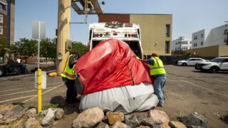 City workers throw a tent into a garbage truck at the end of a forced cleanup at Park Avenue and Curtis Street in Five Points. Aug. 26, 2020.