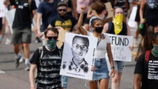 Demonstrators carry placards as they walk down Sable Boulevard during a rally and march over the death of 23-year-old Elijah McClain, Saturday, June 27, 2020, in Aurora, Colo. McClain died in late August 2019 after he was stopped while walking to his apartment by three Aurora Police Department officers.