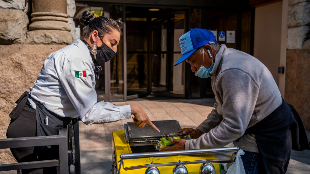 A waitress stops Delgado and picks out a paleta while he’s on his way to a nearby convenience store for refreshments and a break in downtown Denver on Oct. 8, 2020. He sometimes worries about meeting so many people throughout the day during the coronavirus pandemic, but knows he must take the risk to make money to survive.