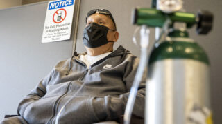 Loren Wilson sits in the waiting room at the Denver Indian Health and Family Services clinic in Sun Valley, breathing from an oxygen tank that he's been using to recover from COVID-19. Nov. 24, 2020.