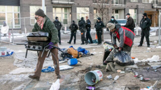 As Denver Police kept a small group of protesters at bay with fencing and, in a few cases, pepper ball rounds and mace, city crews began a sweep of a large homeless encampment at Arkins Court and 29th Avenue in Denver’s RiNo district on Nov. 30, 2020. In this photo, volunteers are helping a man move his belongings as police stand nearby.