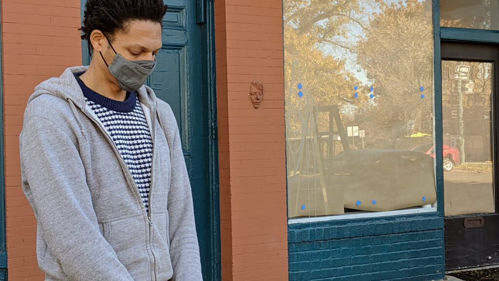 Artist Raafi Rivero stands for a moment of silence on Nov. 1, 2020 before placing four of his memorials to African-American victims of law enforcement violence on the windows of Leon Gallery in Denver. (Donna Bryson/Denverite)