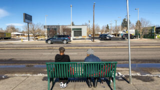 Kristy Jo Gower, right, waits for a bus with someone she just met on East Colfax Avenue, Nov. 25, 2020. Gower said she'd spend a million dollars on helping people experiencing homelessness, like herself. "They need help to stand up," she said. "They don't need a kick in the teeth."