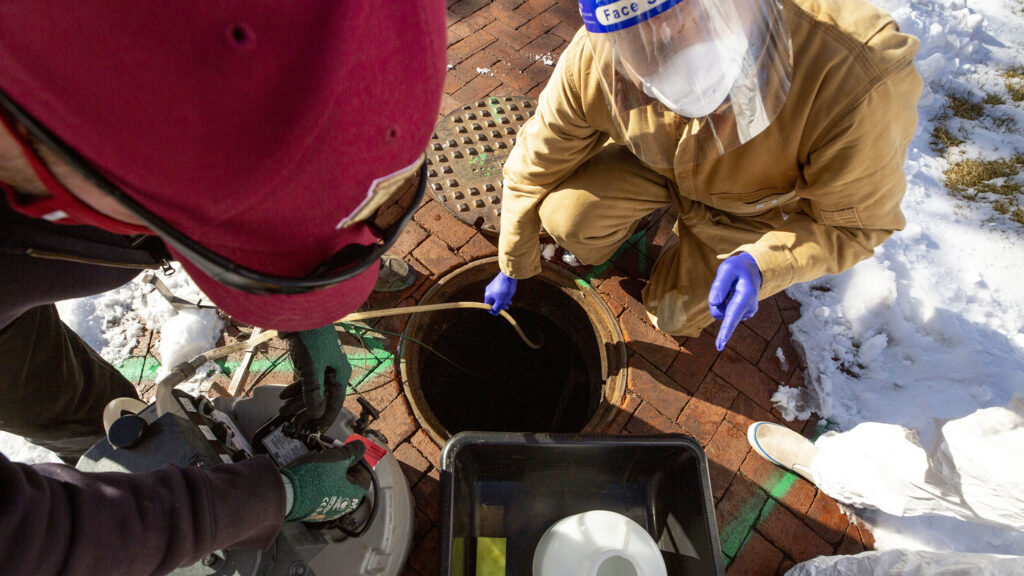 Shawn Martin (left to right), Professor Keith Miller and student Vander Georgeff remove a wastewater sampler from a manhole outside of the University of Denver's Nelson Hall. Dec. 16, 2020.