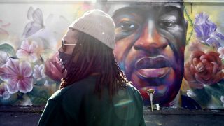 Quincy Shannon, who led some of last summer's Denver protests in the aftermath of George Floyd's killing, pays his respects at the mural of Floyd by artist Detour on Tuesday.